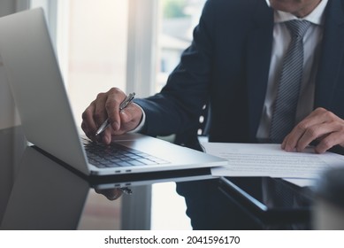 Businessman Working On Laptop Computer With Paper Document On Table At Modern Office. Business Man, Manager Proofing Business Agreement Form Via Laptop. Lawyer Working With Official Contract