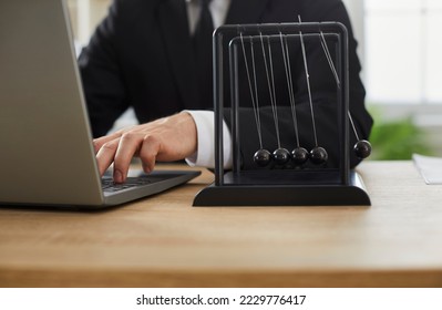 Businessman working on laptop computer at his desk with Newton's cradle. Close up of Newton's pendulum on office table of man typing on notebook PC keyboard. Cropped shot, closeup. Business background