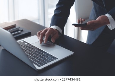 Businessman working on laptop computer at modern office on table, closeup. Business man using mobile phone and typing on laptop, searhing the information, internet networking, corporate business - Powered by Shutterstock