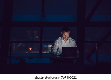 Businessman working on laptop in night office.