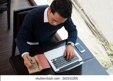 Businessman Working On Laptop And Taking Notes, View From Above