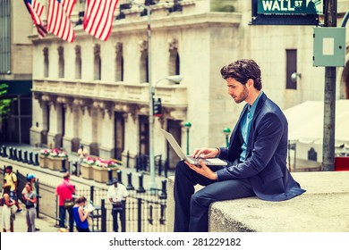 Businessman Working On Street In New York. Dressing In Blue Suit, A Young Guy With Beard, Sitting Outside Office Building, Looking Down, Reading, Typing On Laptop Computer. Instagram Filtered Effect.