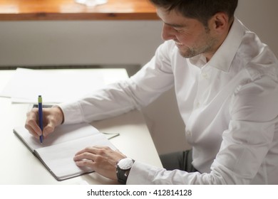 businessman writes in a notebook while sitting at a desk 