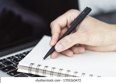 Businessman writes with a pen in diary on laptop keyboard in a sunny office, business and education concept. Close up