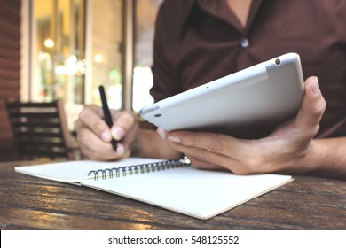 Businessman Writing Notes From Ipad Mini At Coffee Shop. Selective Focus, Over Light And Film Color Tone