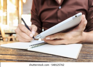 Businessman Writing Notes From Ipad Mini At Coffee Shop. Selective Focus, Over Light