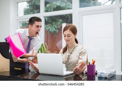 Businessman Yelling At Female Colleague At Desk In Office