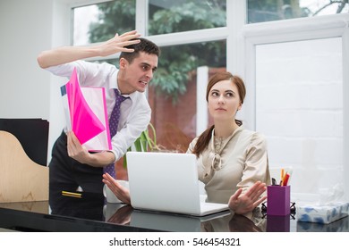 Businessman Yelling At Female Colleague At Desk In Office