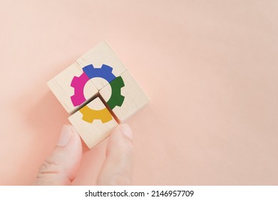 Businessman's hand  arranged wooden cube blocks with multi color of gear icon included copy space on orange background,  for key to success and team work concept