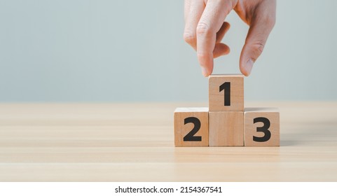 Businessman's Hand Chooses Number 1 On The Podium With Number 2, 3 Of Wooden Building Blocks. Ranking And Strategy Concept. Winners Podium, Business Hierarchy