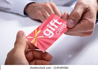 Businessman's Hand Giving Gift Card To His Partner Over Desk