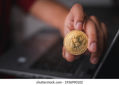 Businessman's hand holding a gold Bitcoin on a laptop. Make money with bitcoin, blockchain transfer