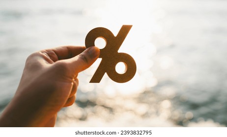 Businessman's hand holding a symbol Percentage with blur sea background, concept of systems of raising or lowering Fed interest rates to correct inflation concepts. - Powered by Shutterstock