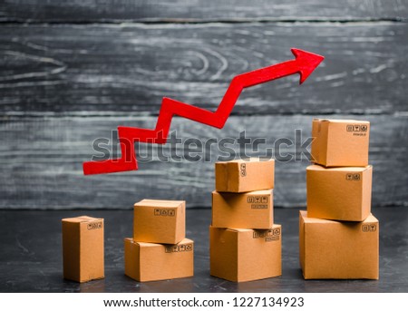 A businessman's hand holds a red arrow up above cardboard boxes folded incrementally. Sales growth and increase in exports of goods and services. Growth profits and the number of buyers.