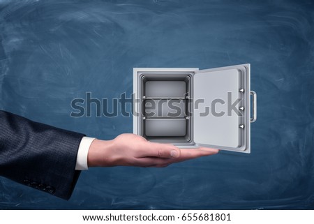 A businessman's hand on blue chalkboard background holding a silver empty safe. Loss of money. Buying stocks. Safekeeping.