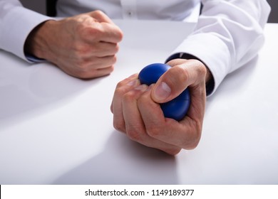 Businessman's Hand Pressing Blue Stress Ball On White Desk