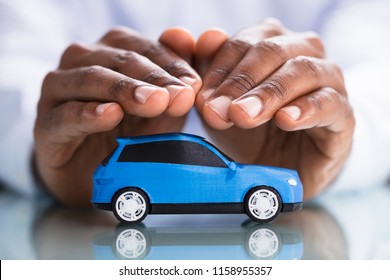 Businessman's Hand Protecting Blue Toy Car On The Reflective Desk - Powered by Shutterstock