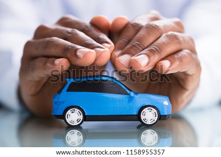 Businessman's Hand Protecting Blue Toy Car On The Reflective Desk