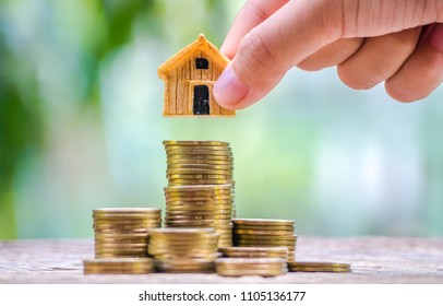 Businessman's hand putting house model on top of coins stack. Concept for loan, property ladder, financial, mortgage, real estate investment, taxes and bonus.