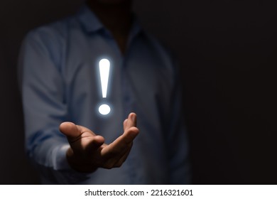 The businessman's hand shows a white exclamation mark. business development concept, error warning, notification, maintenance, and finding a solution. dark background with copy space - Shutterstock ID 2216321601