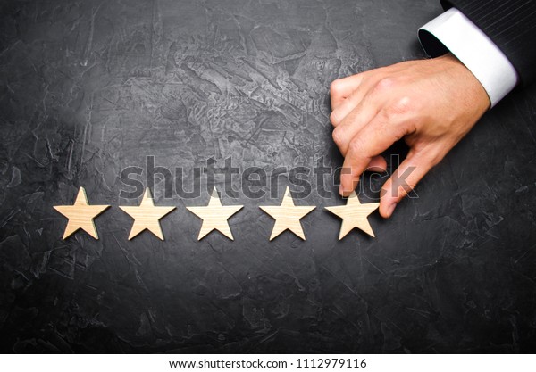 The businessman\'s hand in the suit holds the\
fifth star. Get the fifth star. The concept of the rating of hotels\
and restaurants, the evaluation of critics and visitors. Quality\
level, good service.