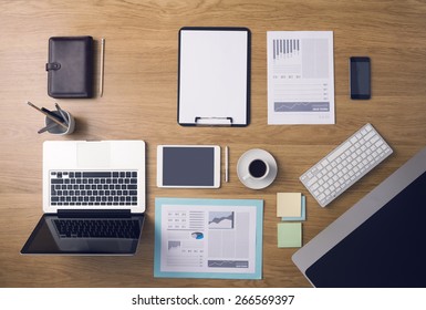 Businessman's Tidy Desktop And Work Tools With Paperwork, Computer, Touch Screen Devices And Stationery On A Wooden Surface, Top View