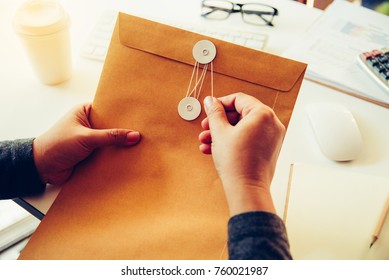 Businessmen Are About To Open A Brown Envelope Containing Business Documents On A Desk With Office Supplies 
