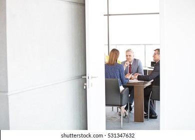 Businessmen And Businesswoman In Board Room Seen Through Open Door At Office