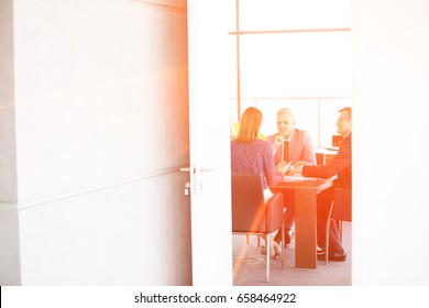 Businessmen And Businesswoman In Board Room Seen Through Open Door At Office