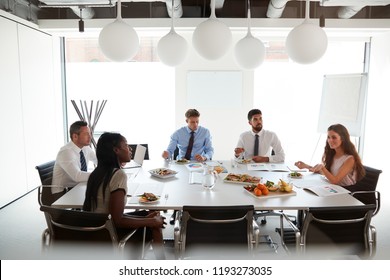 Businessmen And Businesswomen Meeting In Modern Boardroom Over Working Lunch