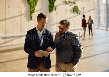 Businessmen cooperating while working on digital tablet in a hallway conference hall. 