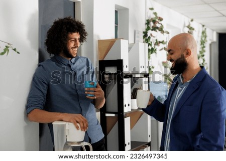 Businessmen enjoying coffee break together and laughing while relaxing in corporate office. Smiling arab young start up company employees mates chatting in coworking space