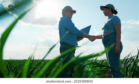 Businessmen farmers teamwork, handshake. Agricultural workers agronomist. Business people shaking hands on green field, teamwork. Man woman farmer checking corn growth analyzing using Digital tablet - Powered by Shutterstock