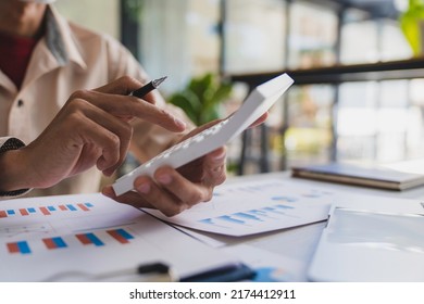 Businessmen hold graph pens and use a calculator for the company's improvement plan. - Shutterstock ID 2174412911