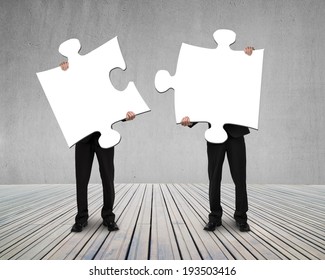 Businessmen Holding Two Puzzles To Connect On Wooden Floor