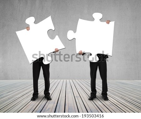 Businessmen holding two puzzles to connect on wooden floor