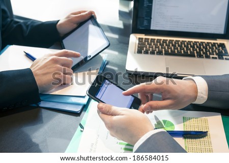 Businessmen at meeting presenting charts on smartphone, tablet and laptop
