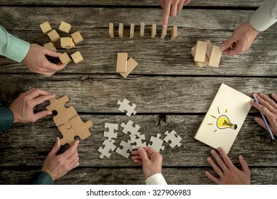 Businessmen planning business strategy while holding puzzle pieces, creating ideas with light bulb drawn on paper and rearranging wooden blocks. Conceptual of teamwork, strategy, vision or education. 