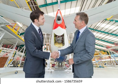 Businessmen Shaking Hands In Aircraft Maintenance Hangar