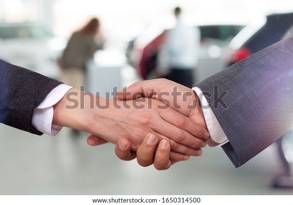 businessmen shaking hands\
in auto showroom