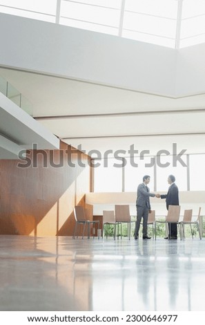 Businessmen shaking hands at circle of chairs in lobby