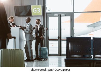 businessmen standing at airport reception to buy tickets while colleague walking to them - Powered by Shutterstock