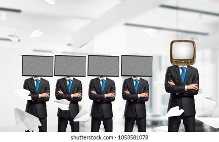 Businessmen in suits with old TV instead of their heads keeping arms crossed while standing in a row and one at the head with TV inside office building.