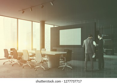 Businessmen talking in corner of panoramic meeting room with gray walls, concrete floor, long white table with gray and white chairs and mock up screen on the wall. Toned image double exposure