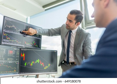 Businessmen trading stocks online. Stock brokers looking at graphs, indexes and numbers on multiple computer screens. Colleagues in discussion in traders office. Business success concept.