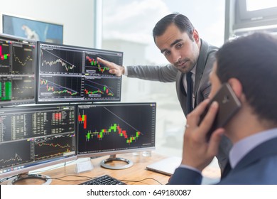 Businessmen Trading Stocks Online. Stock Brokers Looking At Graphs, Indexes And Numbers On Multiple Computer Screens. Colleagues In Discussion In Traders Office. Business Success Concept.