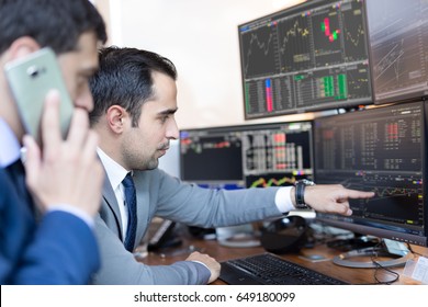 Businessmen trading stocks online. Stock brokers looking at graphs, indexes and numbers on multiple computer screens. Colleagues in discussion in traders office. Business success concept. - Shutterstock ID 649180099