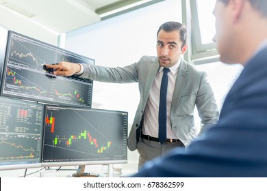 Businessmen Trading Stocks Online. Stock Brokers Looking At Graphs, Indexes And Numbers On Multiple Computer Screens. Colleagues In Discussion In Traders Office. Business Success Concept.