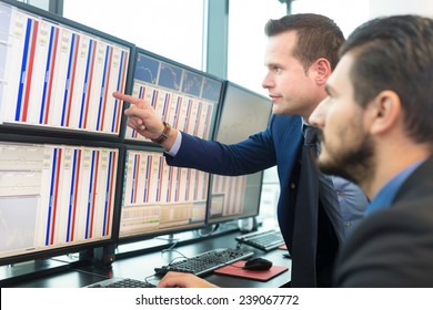 Businessmen trading stocks. Stock traders looking at graphs, indexes and numbers on multiple computer screens. Colleagues in discussion in traders office.  - Powered by Shutterstock