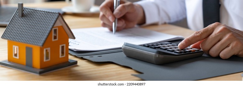 Businessmen Using A Calculator Calculating House Tax Refund On The Table, An Accountant Calculating Tax Report, Financial Concept.